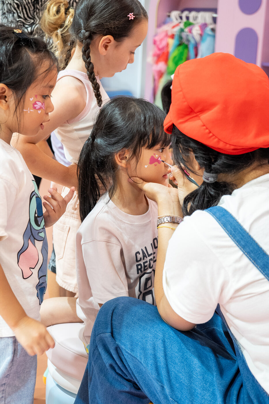 Nanny painting flowers on a girl’s cheek while other children watch