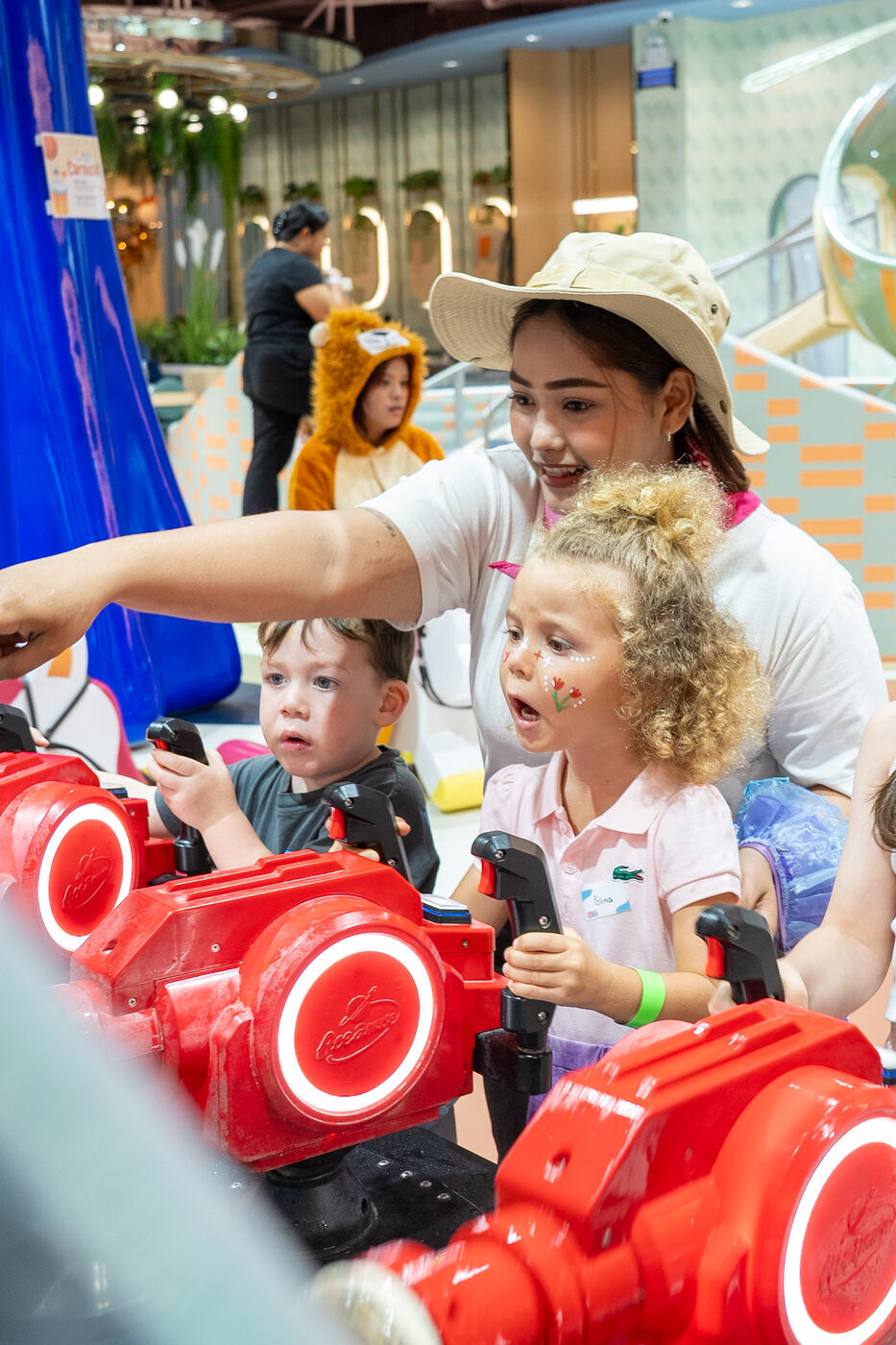Nanny helping two children play on the ride-on machines