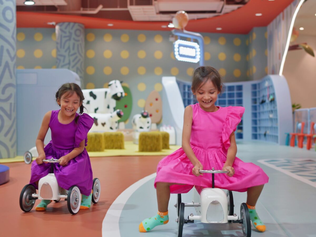 Girls in party dresses riding toy cars around the play park
