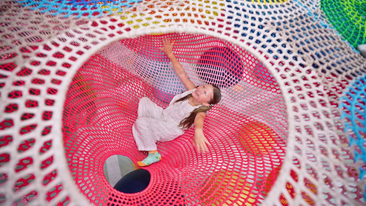 Girl climbing through a colourful net play tunnel