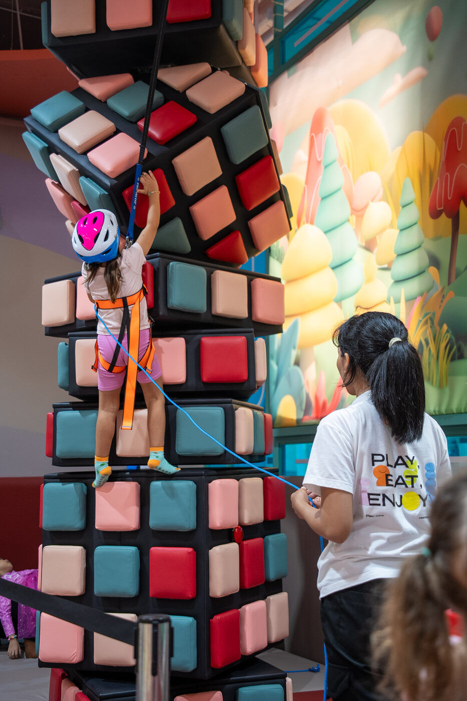 Girl in a helmet and harness climbing the giant cube climbing tower